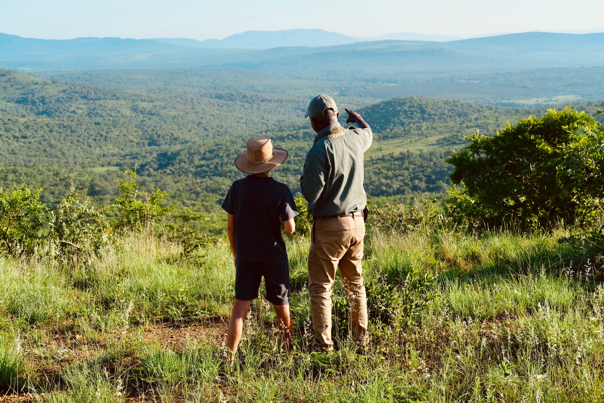 A safari guide and a child looking out over a forested valley