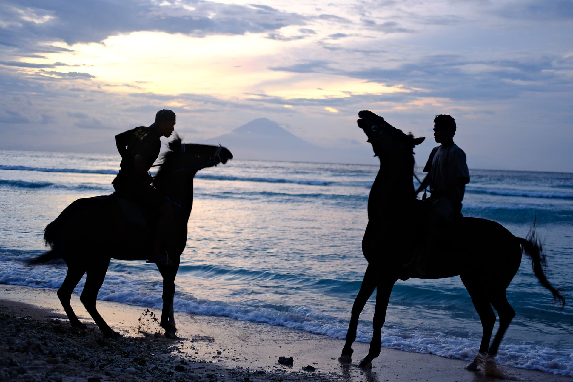 Two riders on horseback along the shoreline at sunset